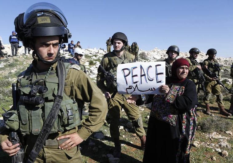 Palestinian protest in West Bank A protester holds a placard as she stands next to Israeli soldiers during a protest against Israeli settlements in Beit Fajjar town south of the West Bank city of Bethlehem. (photo credit:REUTERS)