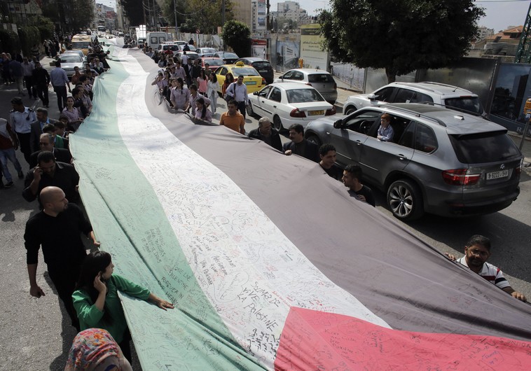 PEOPLE MARCH as they hold a large Palestinian flag in Ramallah in October.